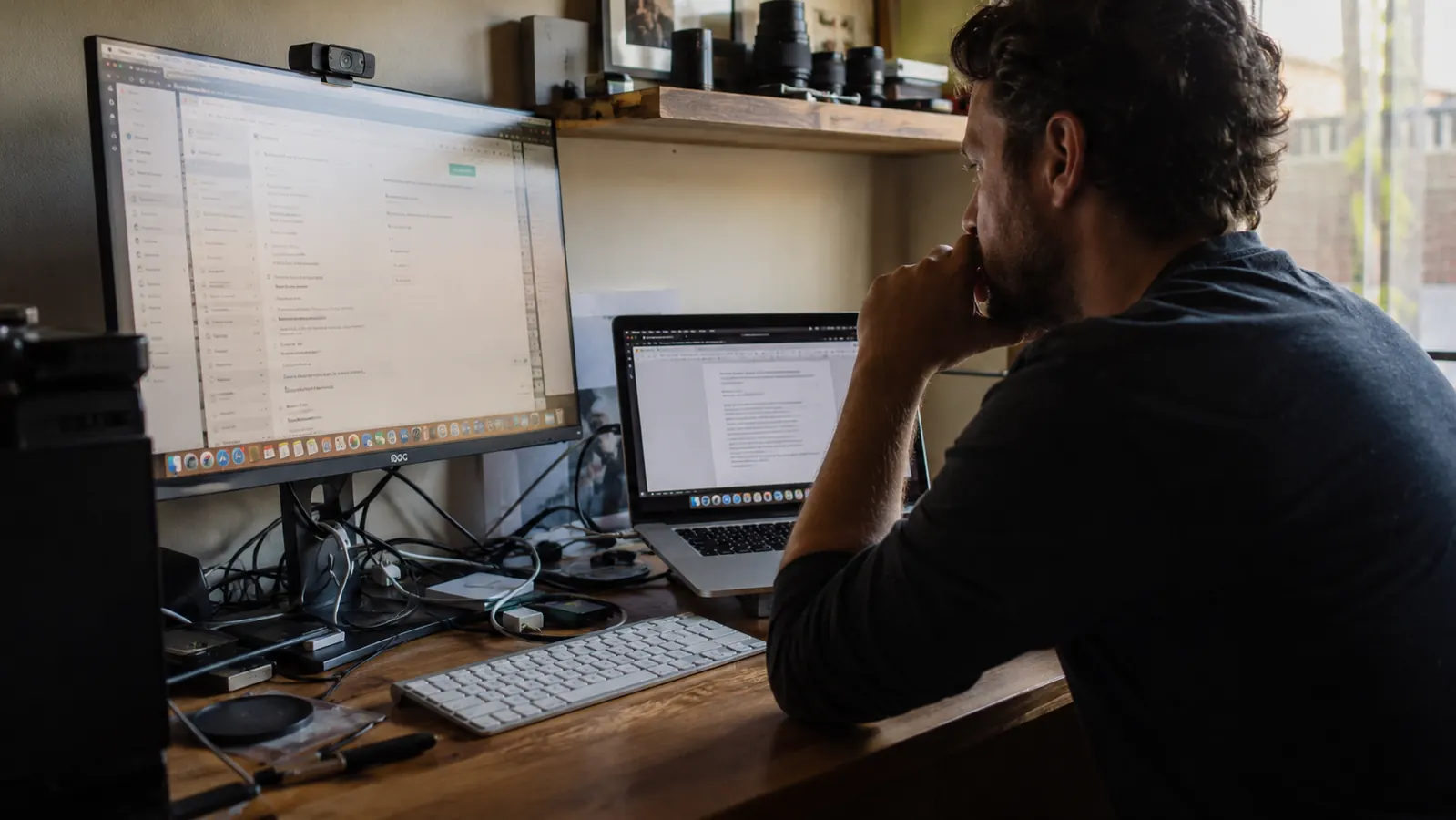 Cluttered home office desk with tangled cords visible behind a monitor, late afternoon light