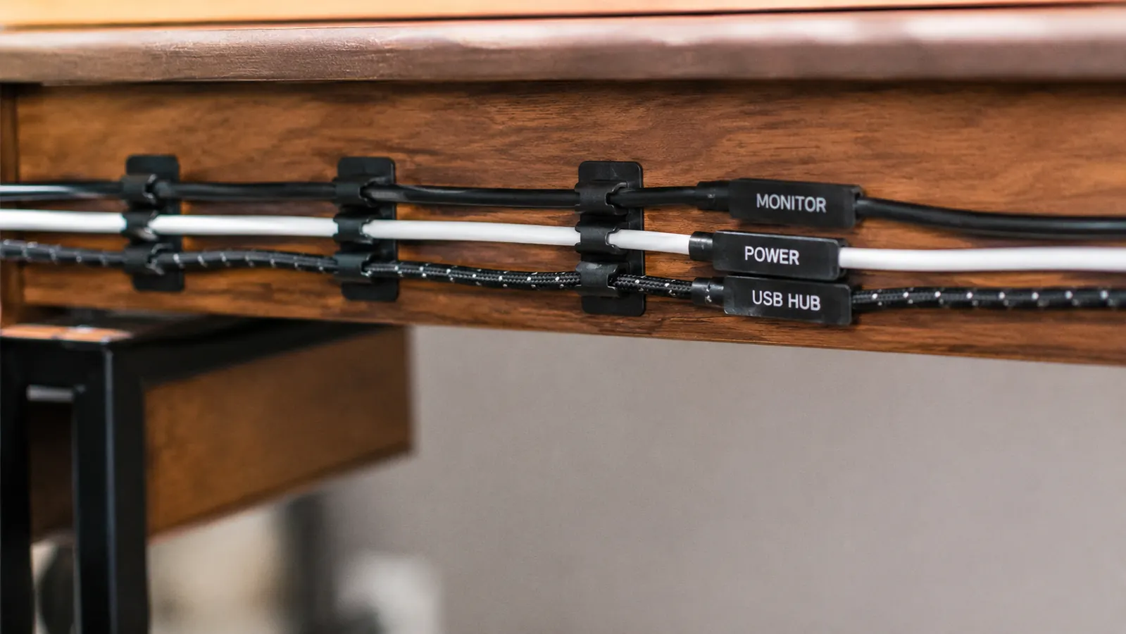 Close-up of cable clips and velcro ties routing monitor, power, and USB cables along the back edge of a desk