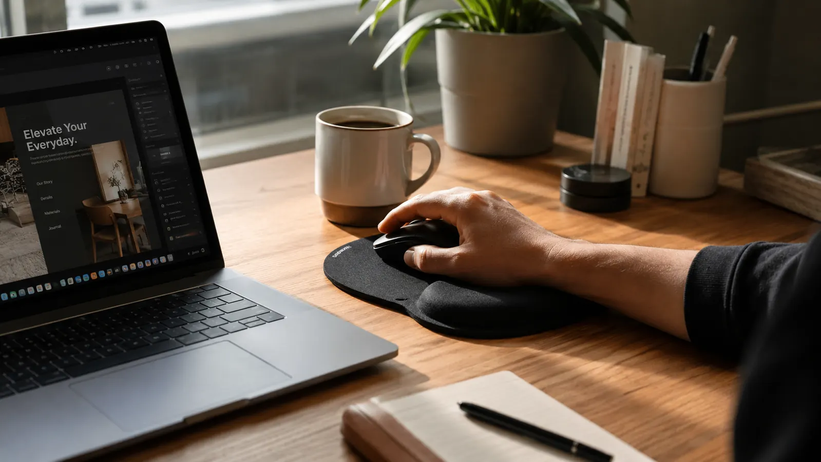 Home office desk with a clean setup, hand resting comfortably on a black ergonomic mouse pad with gel wrist rest near a laptop
